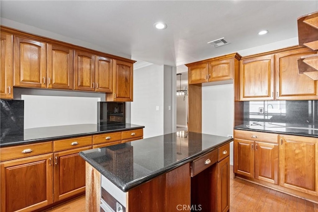 kitchen with tasteful backsplash, visible vents, brown cabinetry, light wood-style flooring, and a center island