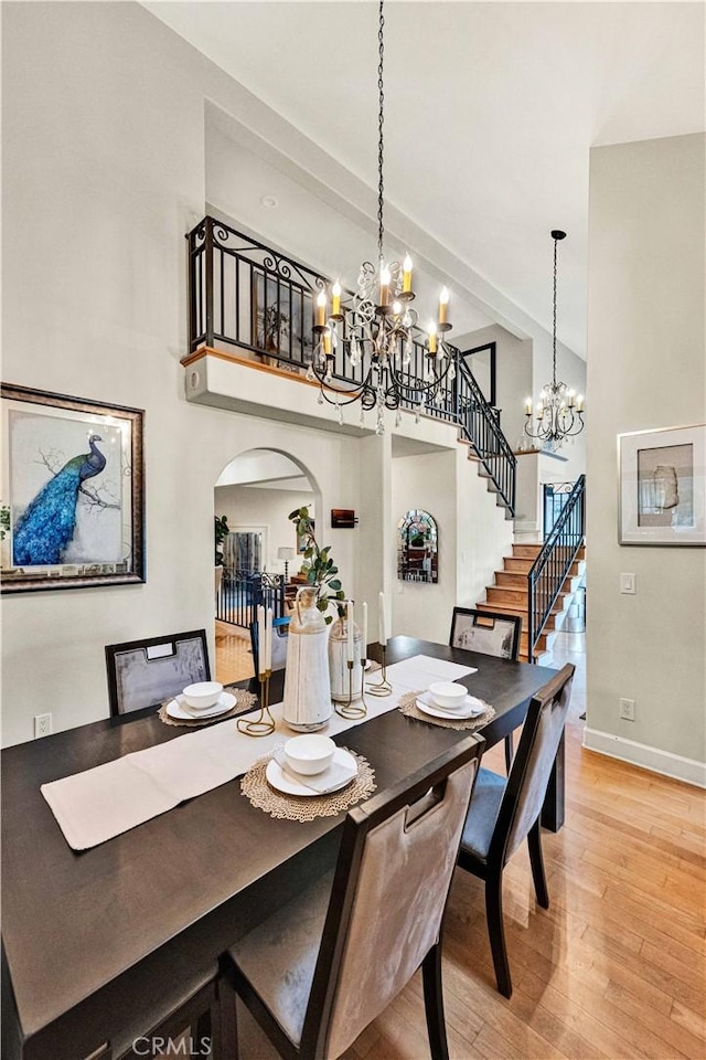 dining space with a towering ceiling, wood-type flooring, and a notable chandelier