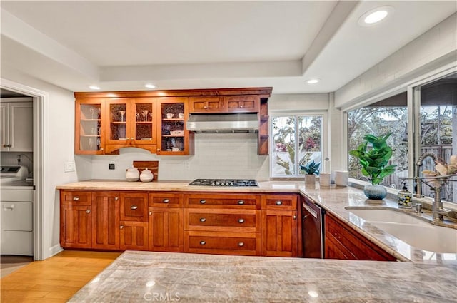 kitchen featuring sink, extractor fan, light stone counters, stainless steel appliances, and washer / clothes dryer