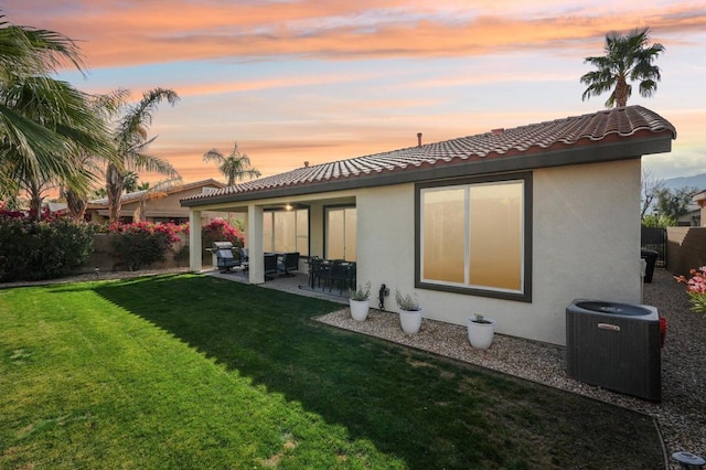 back house at dusk featuring a yard, a patio, and central air condition unit