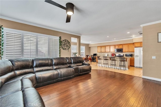 living room with ornamental molding, light hardwood / wood-style floors, and ceiling fan