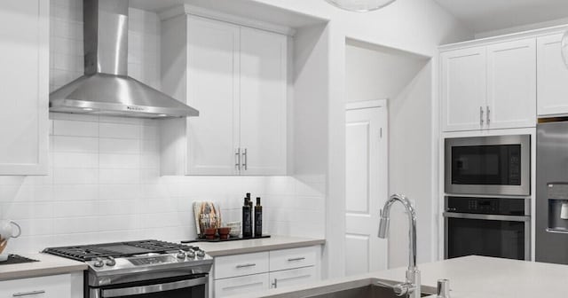 kitchen with white cabinetry, decorative backsplash, wall chimney exhaust hood, and appliances with stainless steel finishes