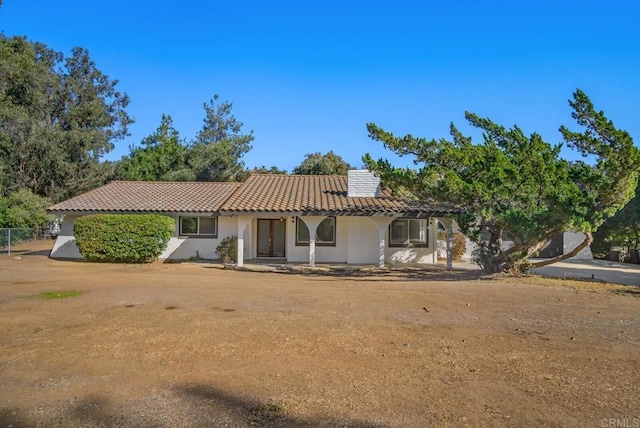 view of front of house featuring stucco siding, a chimney, solar panels, and a tiled roof