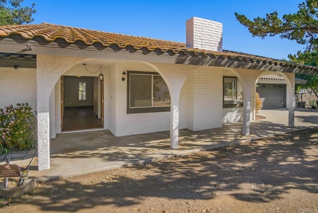 view of exterior entry featuring an attached garage, a tile roof, a chimney, and stucco siding