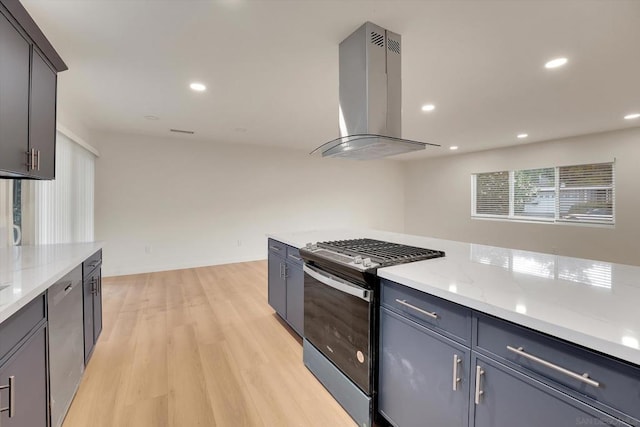 kitchen with gray cabinetry, island exhaust hood, light stone countertops, stainless steel gas range, and light hardwood / wood-style flooring