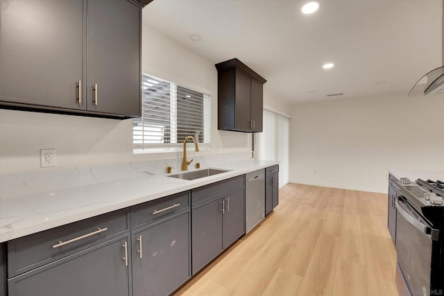 kitchen with dishwasher, sink, range, light stone countertops, and light wood-type flooring