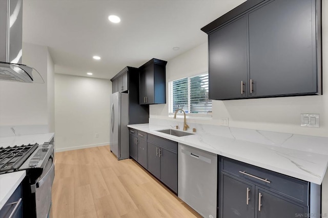 kitchen with sink, appliances with stainless steel finishes, light stone countertops, light hardwood / wood-style floors, and wall chimney range hood