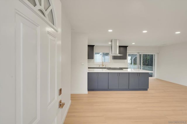 kitchen with island exhaust hood, sink, gray cabinetry, and light hardwood / wood-style floors