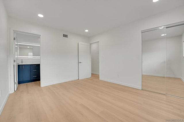 unfurnished bedroom with sink, ensuite bath, light hardwood / wood-style flooring, and a closet