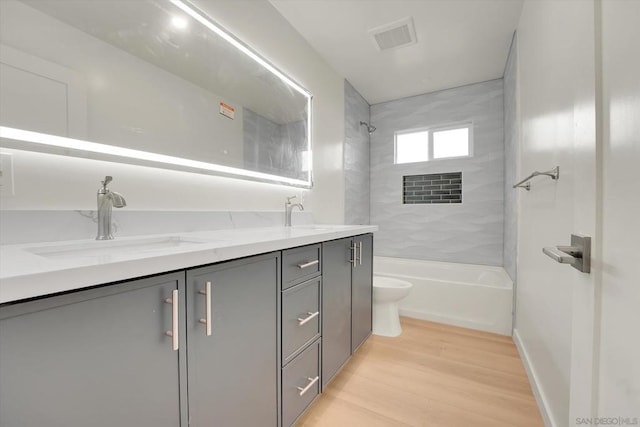 full bathroom with vanity, hardwood / wood-style floors, tiled shower / bath, and toilet