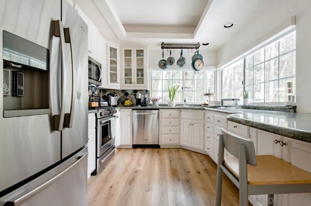 kitchen with dark stone countertops, appliances with stainless steel finishes, a raised ceiling, and white cabinets