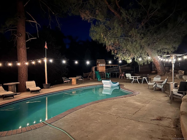 pool at night featuring a playground and a patio area