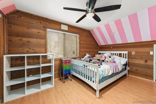 bedroom with lofted ceiling, light hardwood / wood-style floors, ceiling fan, and wood walls