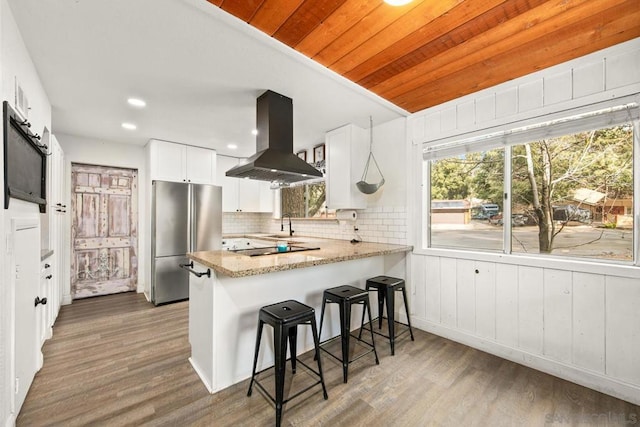 kitchen featuring white cabinetry, wood ceiling, stainless steel fridge, kitchen peninsula, and island exhaust hood