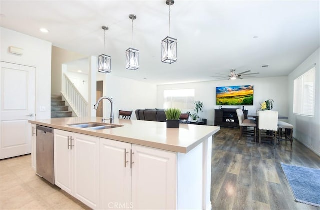 kitchen featuring decorative light fixtures, sink, white cabinets, stainless steel dishwasher, and a center island with sink