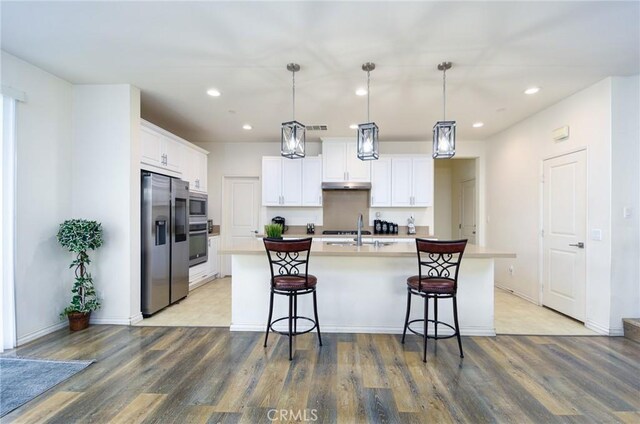 kitchen featuring stainless steel appliances, white cabinetry, a center island with sink, and decorative light fixtures