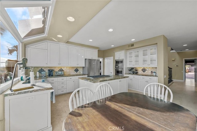 kitchen featuring stainless steel appliances, a center island, light stone countertops, and white cabinets