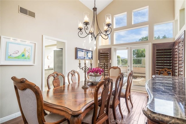 dining room featuring wood-type flooring, a towering ceiling, an inviting chandelier, and french doors