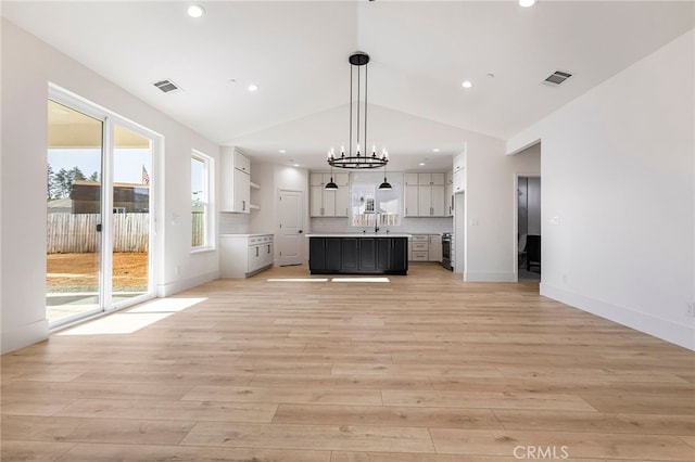 unfurnished living room featuring sink, light hardwood / wood-style floors, vaulted ceiling, and a notable chandelier