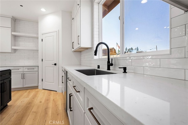 kitchen featuring sink, white cabinetry, tasteful backsplash, light wood-type flooring, and light stone countertops