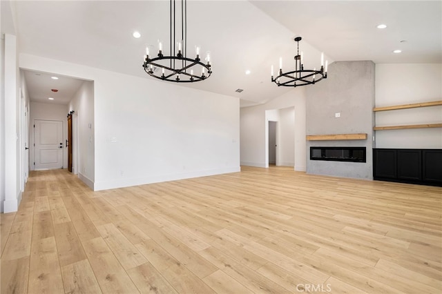 unfurnished living room with high vaulted ceiling, light hardwood / wood-style floors, a large fireplace, and a chandelier