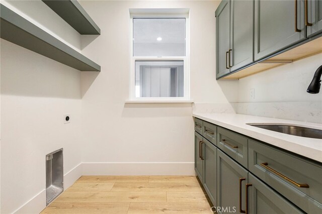 laundry area featuring electric dryer hookup, sink, light hardwood / wood-style floors, and cabinets