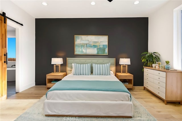 bedroom with ensuite bathroom, a barn door, and light wood-type flooring