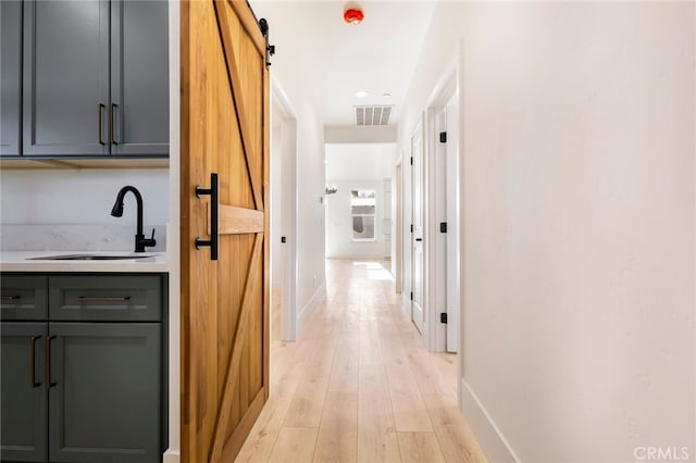 hallway featuring a barn door, sink, and light wood-type flooring