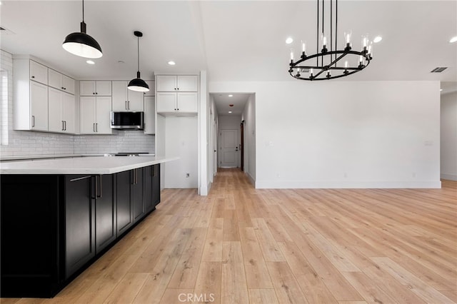 kitchen featuring white cabinetry, tasteful backsplash, a center island, light wood-type flooring, and pendant lighting