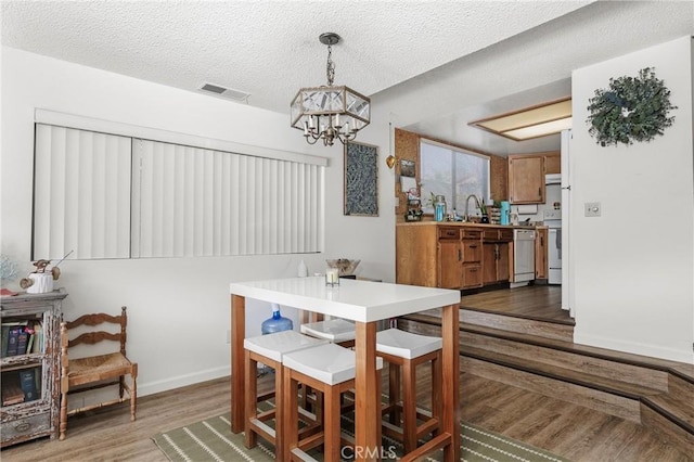 dining space with wood-type flooring, sink, a notable chandelier, and a textured ceiling