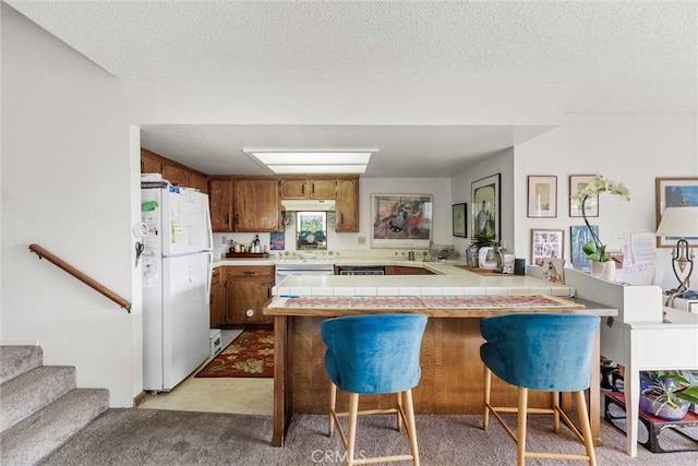 kitchen with white refrigerator, tile counters, a kitchen bar, light carpet, and kitchen peninsula