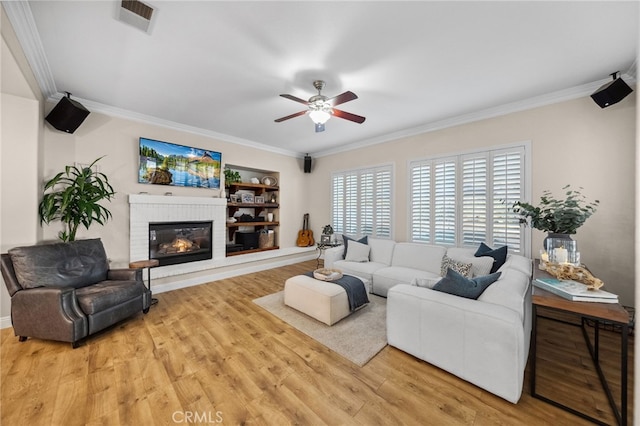 living room with crown molding, a brick fireplace, wood-type flooring, and ceiling fan