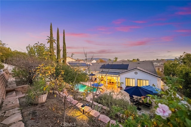 back house at dusk with a patio and solar panels