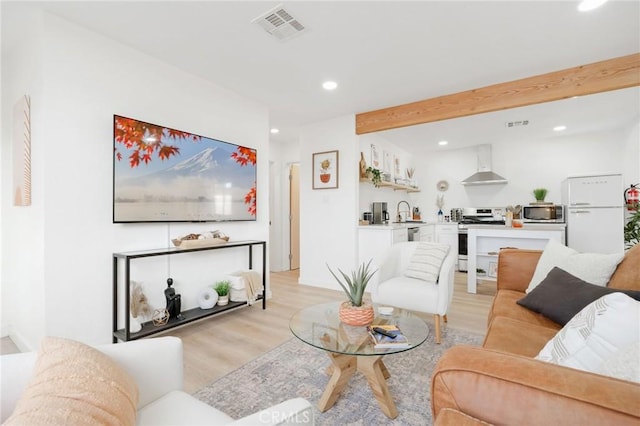 living room featuring beam ceiling, sink, and light wood-type flooring