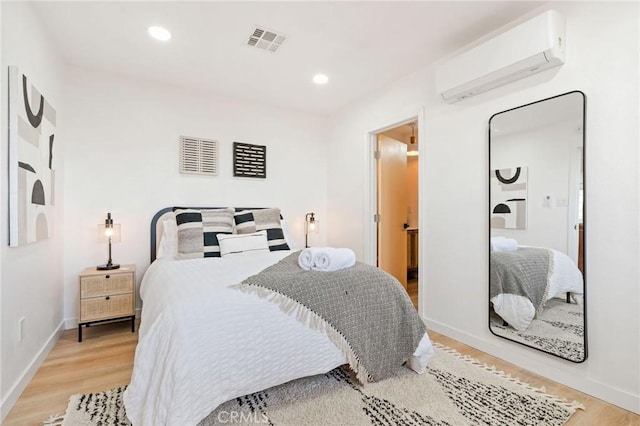 bedroom featuring a wall mounted AC and light hardwood / wood-style floors