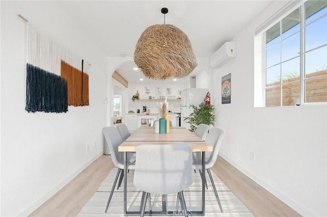 dining area with a wall mounted AC and light wood-type flooring