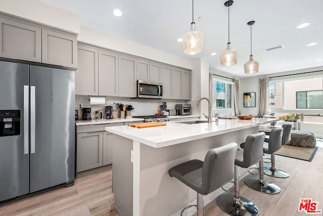 kitchen with gray cabinetry, sink, stainless steel appliances, and a breakfast bar