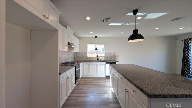 kitchen with tasteful backsplash, appliances with stainless steel finishes, dark stone counters, and white cabinets