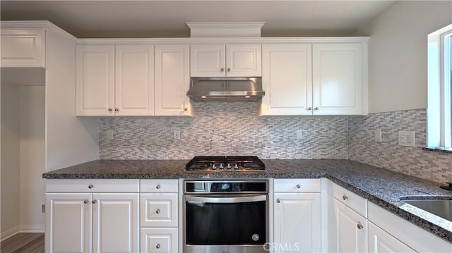 kitchen featuring dark stone countertops, stainless steel appliances, tasteful backsplash, ventilation hood, and white cabinets