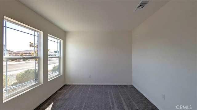 spare room featuring plenty of natural light and dark carpet