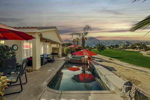 pool at dusk featuring ceiling fan, a mountain view, and a patio