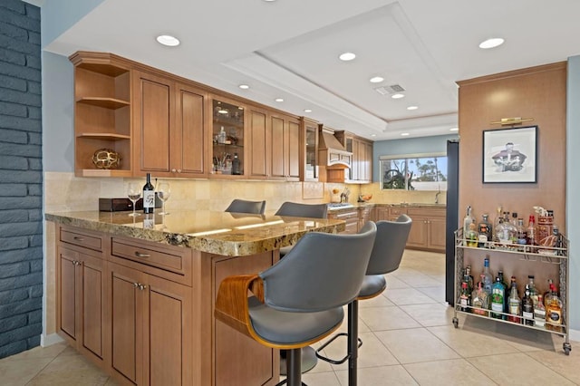 bar featuring light stone countertops, a tray ceiling, wall chimney range hood, and light tile patterned floors