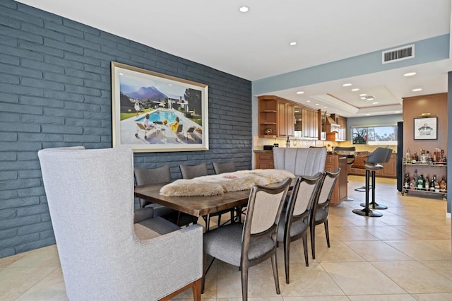 tiled dining area with a raised ceiling and brick wall