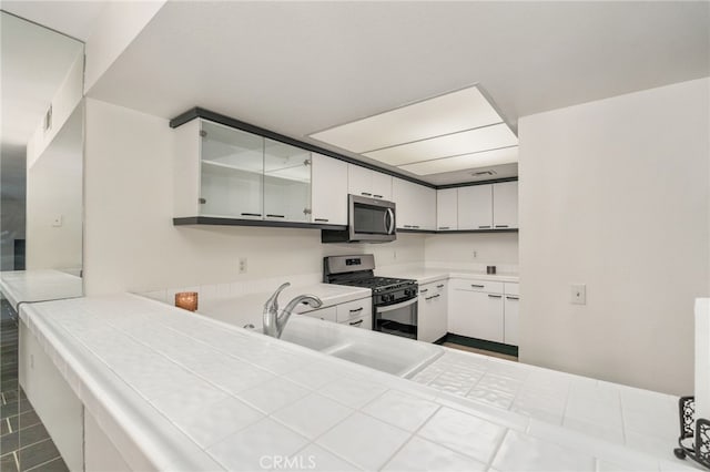 kitchen with sink, tile countertops, white cabinets, and appliances with stainless steel finishes