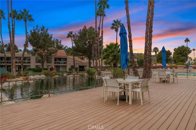 deck at dusk featuring a community pool and a water view