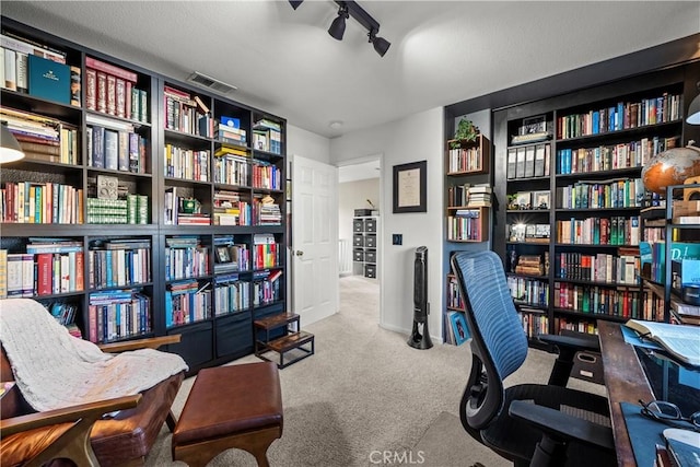 office area featuring light carpet, wall of books, rail lighting, and visible vents