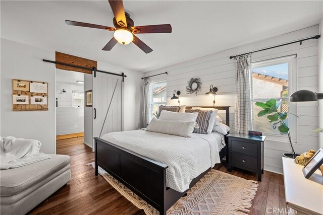 bedroom with ceiling fan, a barn door, dark hardwood / wood-style flooring, and multiple windows