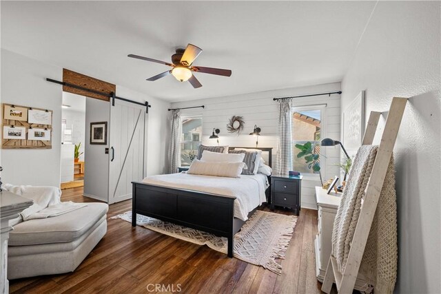 bedroom with dark hardwood / wood-style floors, ceiling fan, and a barn door