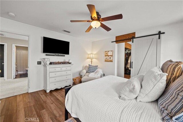 bedroom with a walk in closet, a closet, ceiling fan, a barn door, and light hardwood / wood-style floors