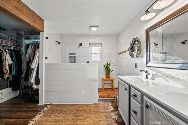 bathroom with double vanity, wood finished floors, a spacious closet, a tile shower, and a sink